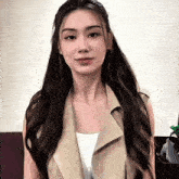 a woman with long hair is wearing a tan vest