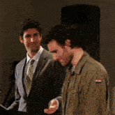 a man in a suit and tie stands next to another man in a military jacket