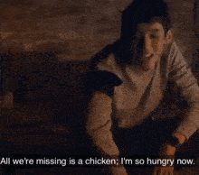 a man is sitting in front of a brick wall with a caption that says all we 're missing is a chicken