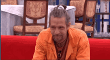 a man with long hair and a beard is sitting on a red couch in front of a table and chairs
