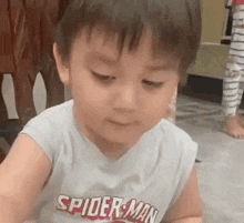 a young boy wearing a spider-man shirt is sitting on the floor .
