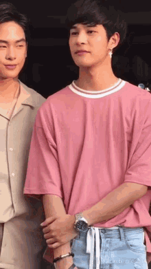 a man in a pink shirt is standing next to another man in a beige shirt .