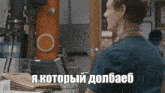 a man in a blue shirt is sitting in front of a machine with the words i 'm looking at a machine in russian