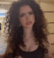 a woman with curly hair and a black tank top makes a funny face