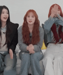 three women are sitting on a couch and one of them is covering her face with her hands .