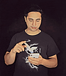 a man wearing a black shirt that says ari looks at his phone