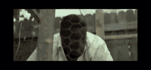a man with a beehive on his face is standing next to a tree .
