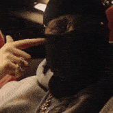 a man wearing a mask and sunglasses is sitting in a car and pointing at his face .