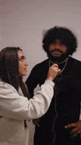 a woman is talking into a microphone while standing next to a man with a beard
