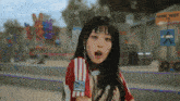 a girl with long black hair is wearing a red and white adidas shirt and making a funny face .