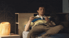 a man in a striped shirt is sitting on a bed looking at his phone