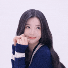 a woman in a blue and white striped sweater is making a heart shape with her hands
