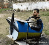 a man sits in a blue and yellow barrel with a propeller on it