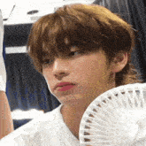a young man is holding a fan in his hand while making a funny face .