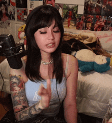 a woman wearing headphones and a blue tank top is sitting on a bed in front of a microphone .
