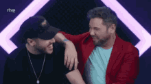 a man in a red jacket is hugging another man in a black hat with the word rtve on the bottom