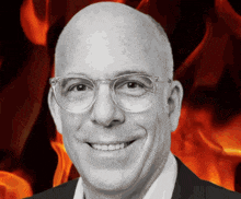 a man wearing glasses and a suit smiles in front of a fire background
