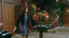 a woman in a dress is standing in front of a table with flowers on it