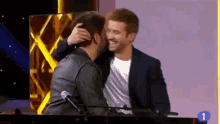 two men are standing next to each other on a stage and hugging .
