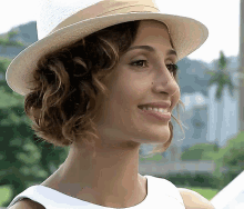 a woman wearing a hat and a white dress smiles for the camera