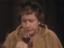 a woman in a brown coat is drinking from a wine glass