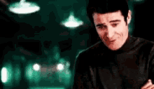 a man in a black turtleneck sweater is smiling in a dark room .