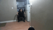 a man in a black shirt sits in a chair in front of a white refrigerator