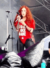 a woman wearing a red shirt that says good luck babe sings into a microphone