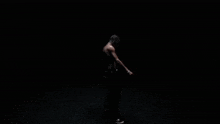 a shirtless man is standing in the dark smoking a cigarette .