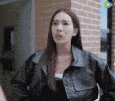 a woman wearing a black leather jacket is standing in front of a brick wall