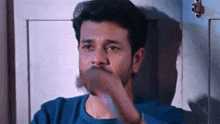 a man with a beard and a blue shirt is covering his mouth with his hand