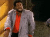 a man with a beard wearing a red shirt and a grey jacket