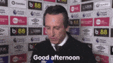a man says good afternoon while standing in front of a wall full of advertisements