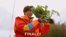 a man in a red jacket is holding a large bunch of green vegetables .