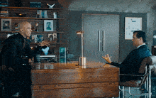 two men are sitting at a desk and talking