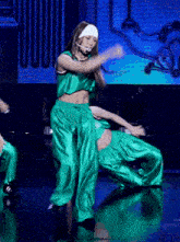 a woman in a green crop top and green pants is dancing on stage