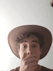 a man wearing a cowboy hat is covering his mouth with his hand