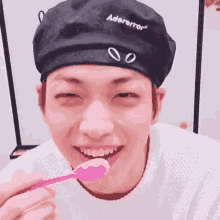 a young man wearing a black beret is eating a pink spoon .