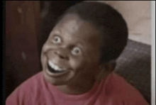 a young boy in a red shirt is smiling with his eyes wide open