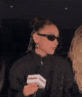 a woman wearing sunglasses is laughing while holding a box and a red circle