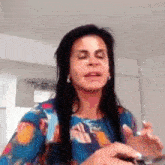 a woman with long black hair is wearing a colorful shirt and holding a knife .