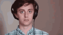 a young man wearing headphones and a plaid shirt is making a surprised face .