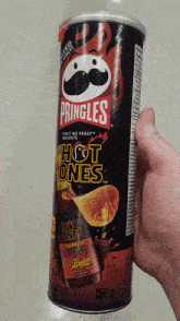 a hand is holding a can of pringles hot ones chips