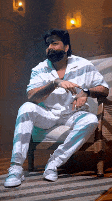 a man with a beard sits in a chair with his hands on his hips
