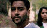 a man with a beard and a woman in the background .