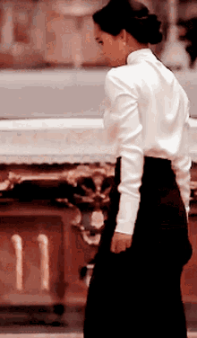 a woman in a white shirt and black skirt stands in front of a statue