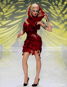 a woman in a red dress with a scarf around her head is standing on a runway