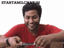 a man in a red shirt is smiling while rolling a cigarette with the words starttamilchat.in above him