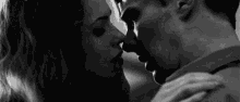 a black and white photo of a man and a woman kissing .