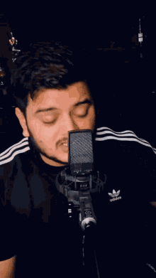 a man singing into a microphone with an adidas shirt on